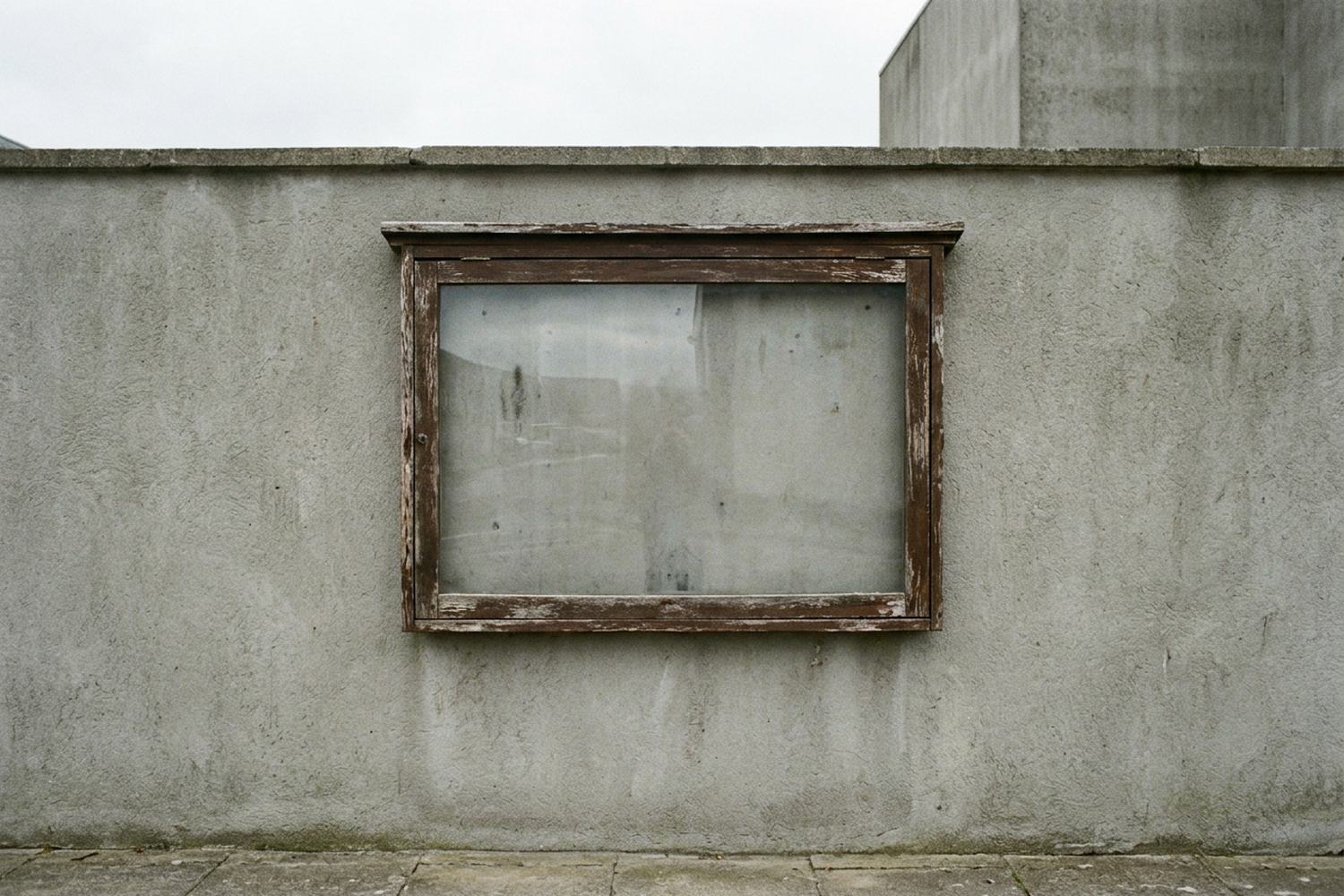 A weathered noticeboard behind glass, empty.