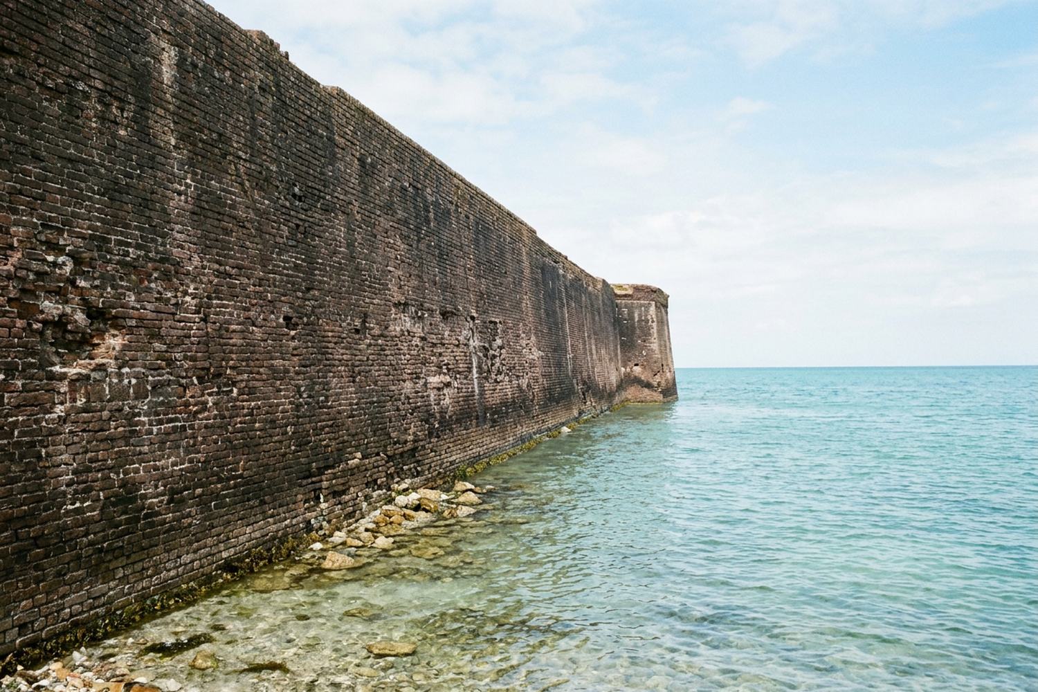 A long brick fortress wall meeting shallow clear water.